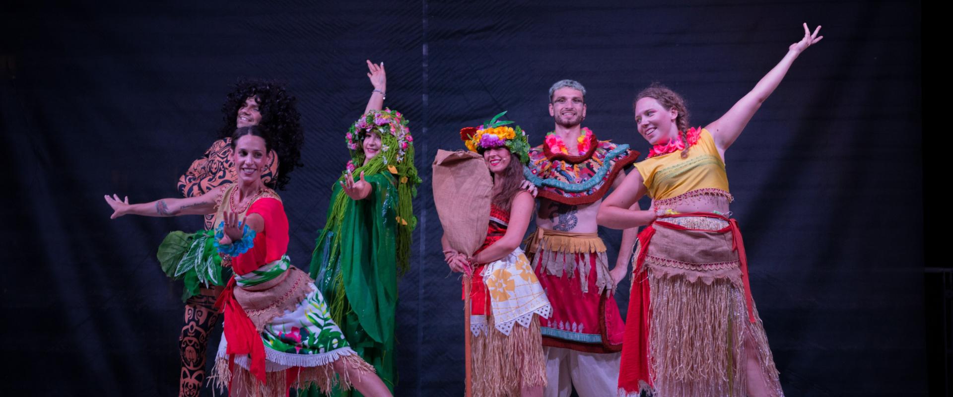 Gruppo in costumi colorati, ispirati a culture polinesiane, posa su un palco.