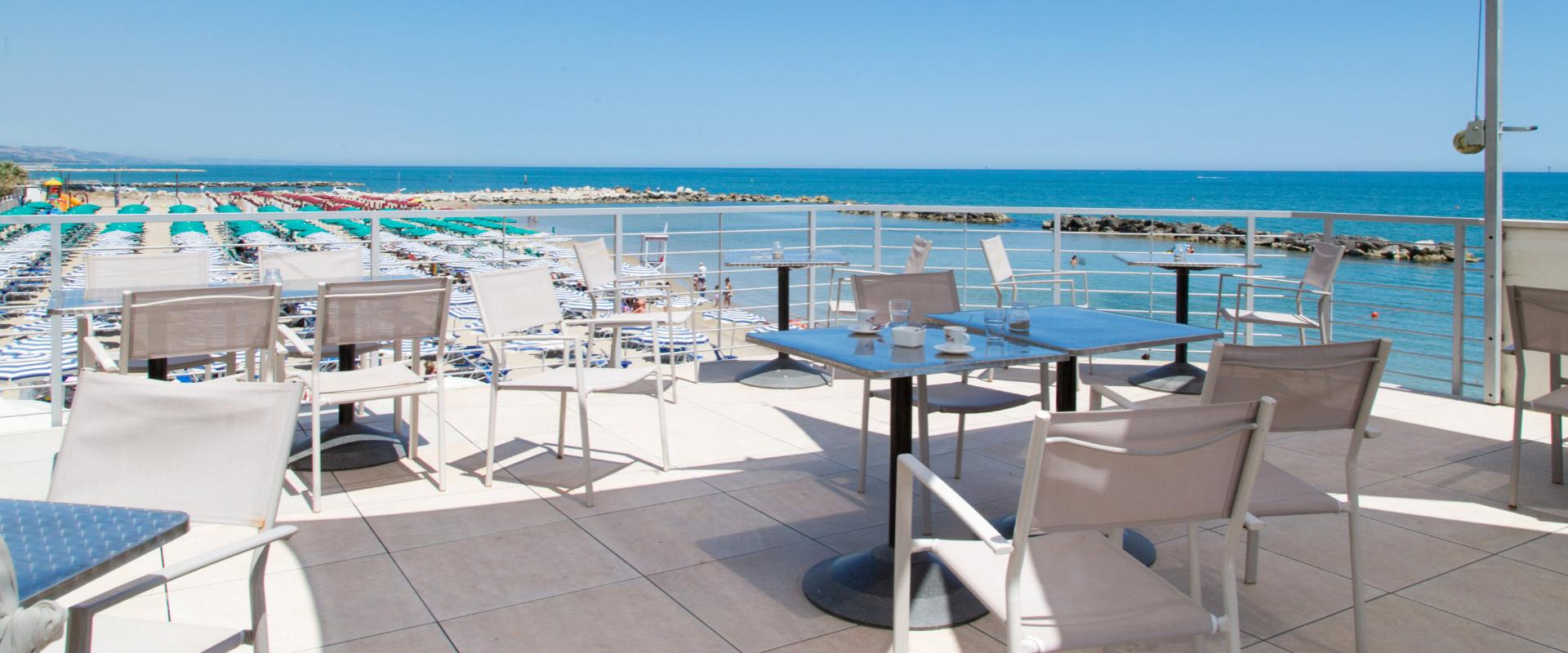 Terrazza con vista mare, sedie e tavoli, spiaggia attrezzata con ombrelloni colorati.