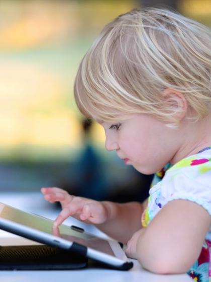 Bambina bionda gioca con tablet, concentrata e curiosa.