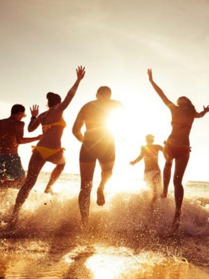 Persone felici corrono verso il mare al tramonto, spruzzi d'acqua e sole.