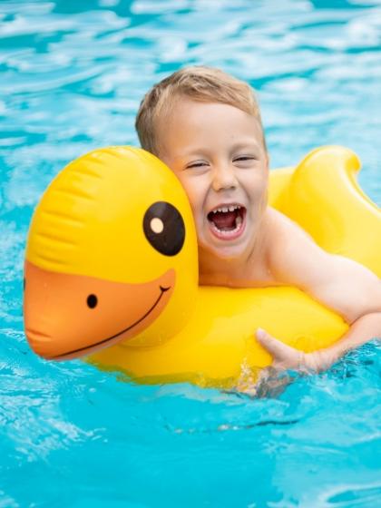 Bambino felice su un gonfiabile a forma di anatra in piscina.
