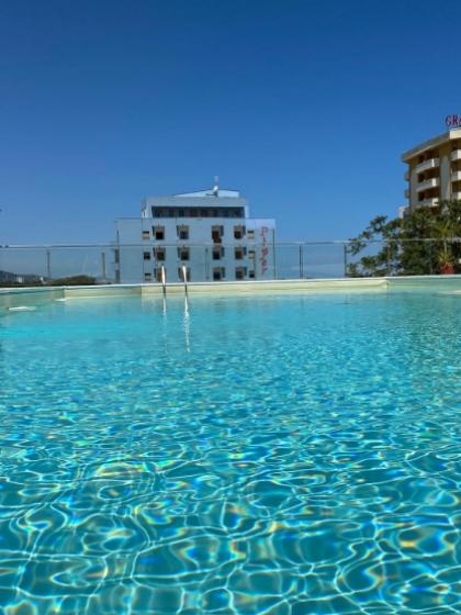Piscina limpida con vista su edifici moderni sotto un cielo azzurro.