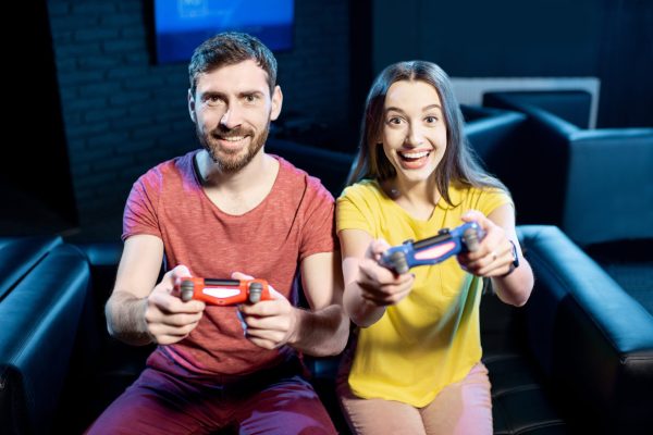 Young couple playing video games with gaming console sitting together on the couch in the dark room